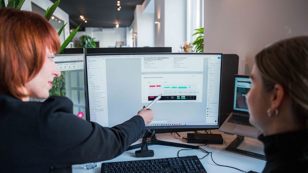Zwei Frauen arbeiten konzentriert an einem Computer in einem modernen Büro.