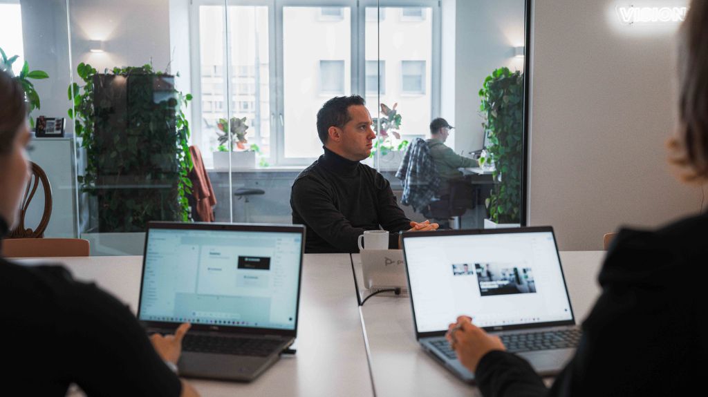Ein Mann sitzt an einem Tisch mit zwei Laptops, konzentriert auf seine Arbeit.